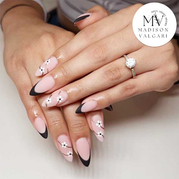 Almond nails in blush pink with black French tips, tiny white daisies and fine gold swirls